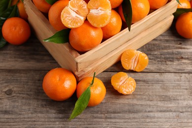 Delicious tangerines with leaves on wooden table, above view