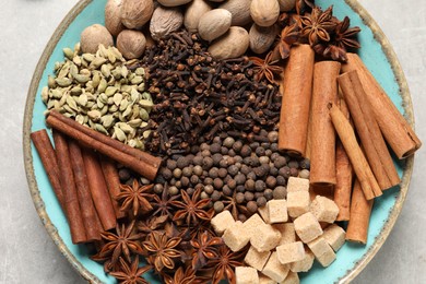 Different spices and nuts in bowl on light gray table, top view