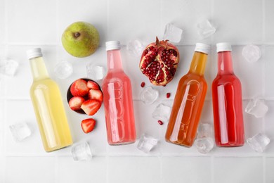 Tasty kombucha in glass bottles, fresh fruits and ice on white table, flat lay