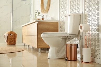 Photo of Toilet bowl near wooden screen in modern bathroom interior