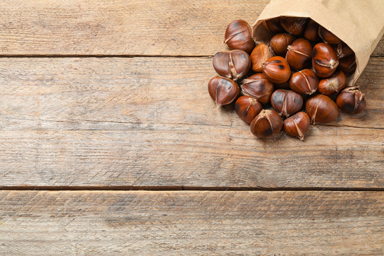 Photo of Delicious roasted edible chestnuts in paper bag on wooden table. Space for text