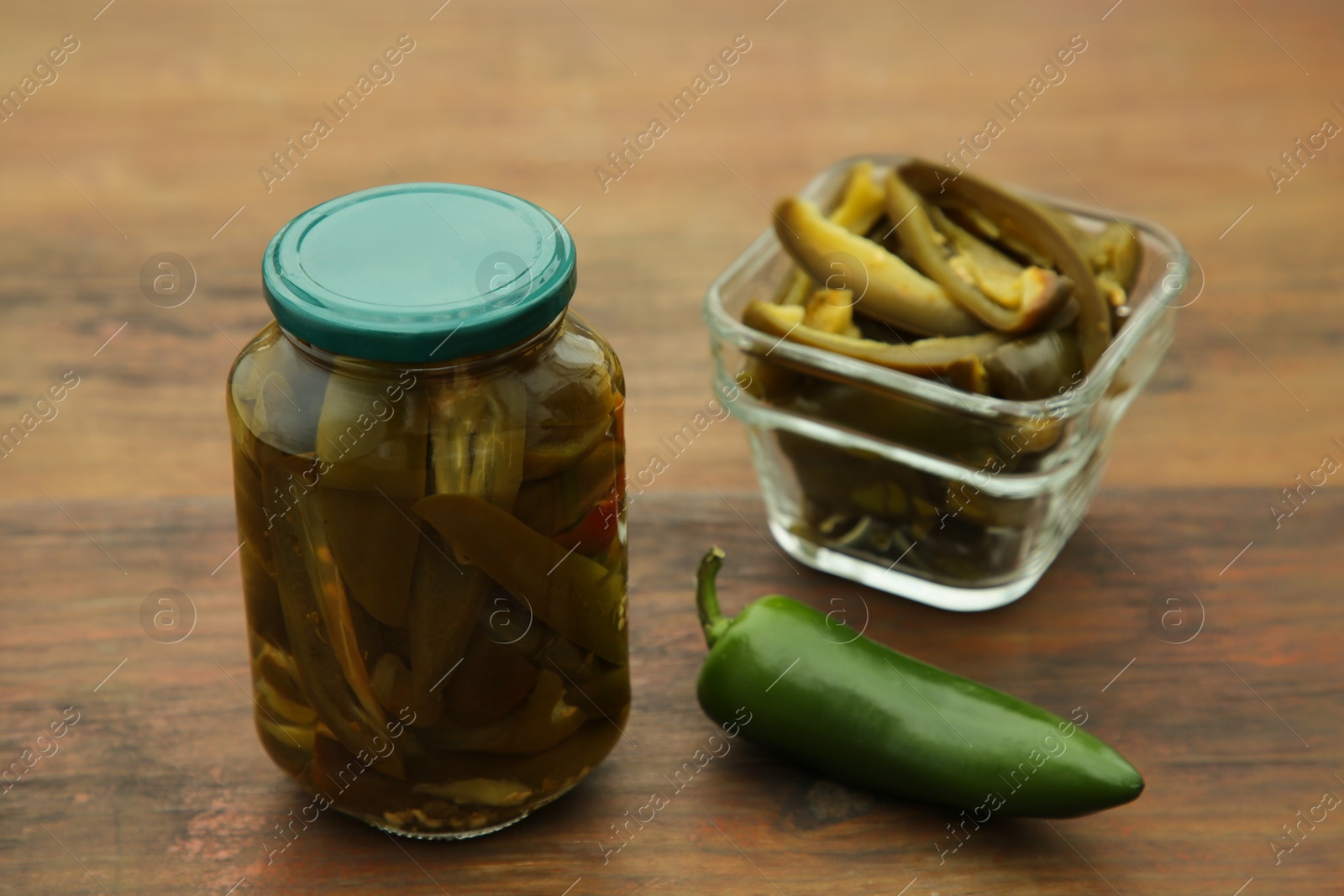 Photo of Fresh and pickled green jalapeno peppers on wooden table