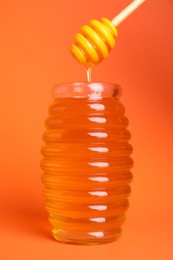 Jar of organic honey and dipper on orange background