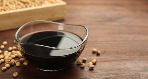 Photo of Soy sauce in bowl and soybeans on wooden table, closeup. Space for text