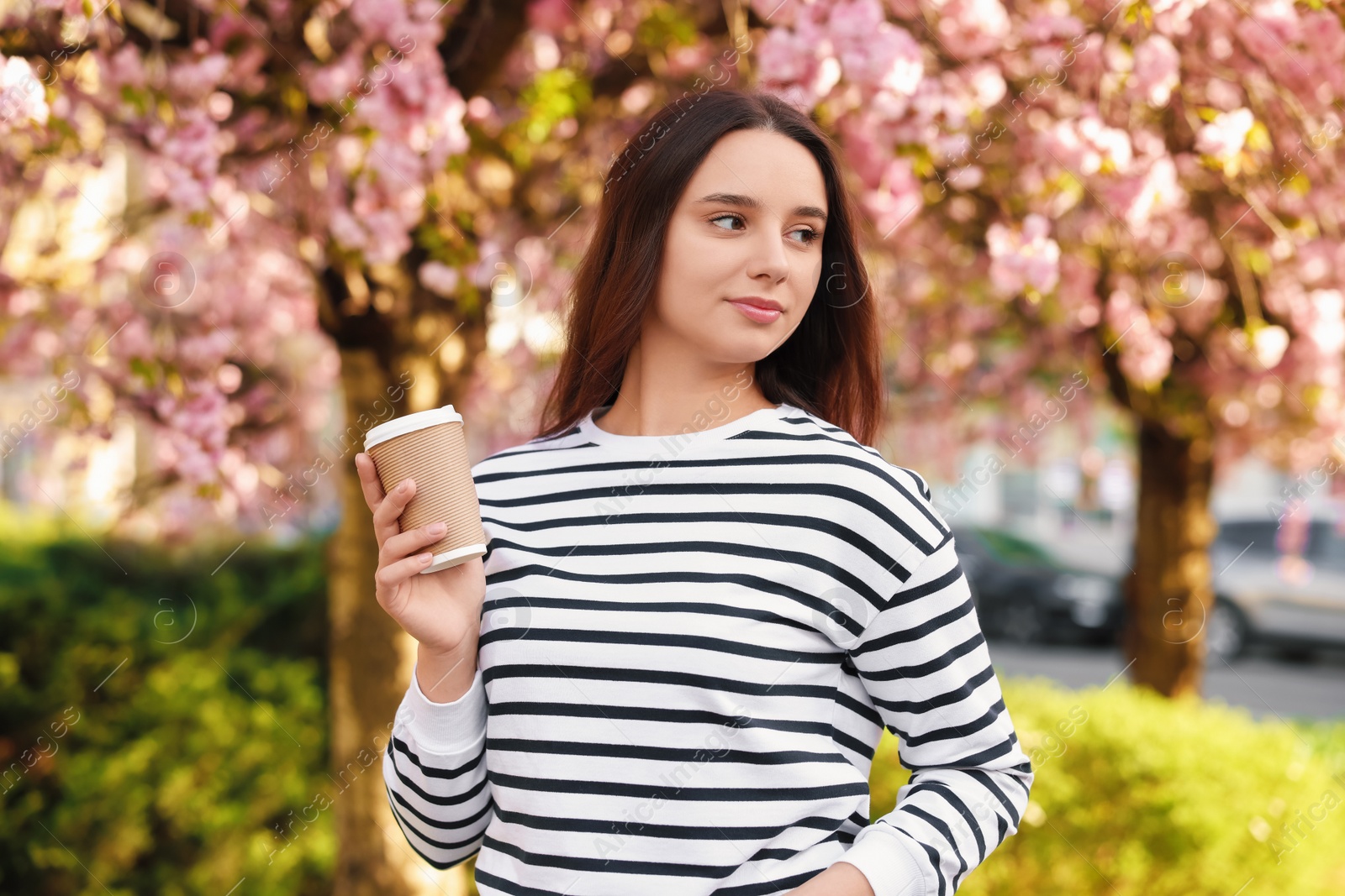 Photo of Beautiful woman with cup of coffee near blossoming tree on spring day