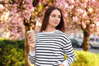 Beautiful woman with cup of coffee near blossoming tree on spring day