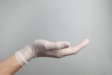 Doctor wearing white medical glove holding something on grey background, closeup