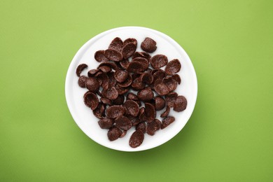 Breakfast cereal. Chocolate corn flakes and milk in bowl on light green background, top view