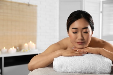 Beautiful Asian woman lying on massage table in spa salon. Space for text