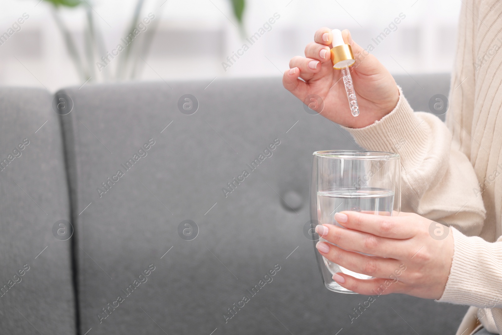 Photo of Woman dripping food supplement into glass of water indoors, closeup. Space for text