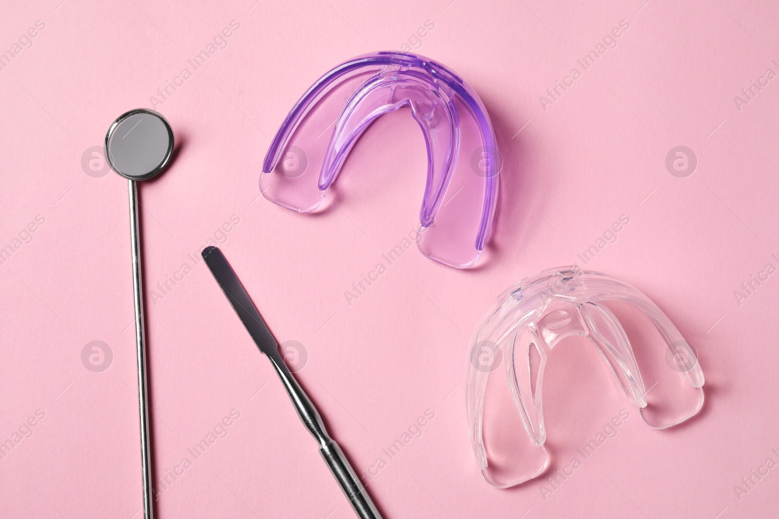 Photo of Bite correction. Transparent mouth guards and dentist tools on light pink background, flat lay