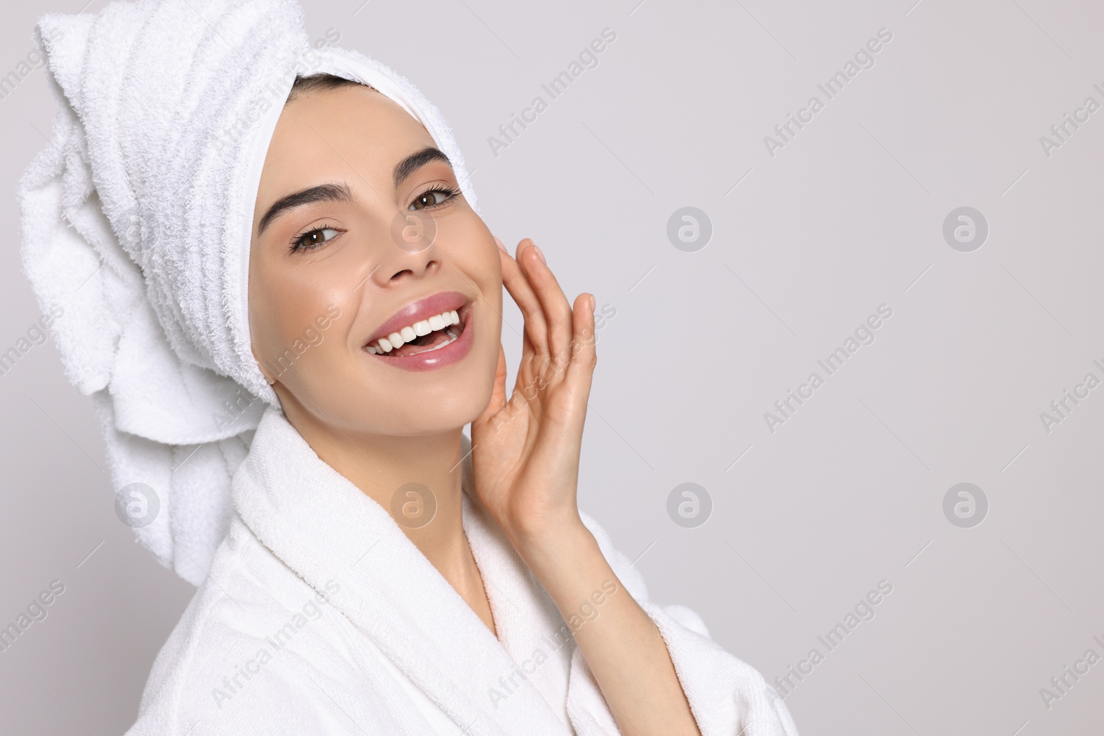 Photo of Young woman in bathrobe with towel on light grey background, space for text. Spa treatment