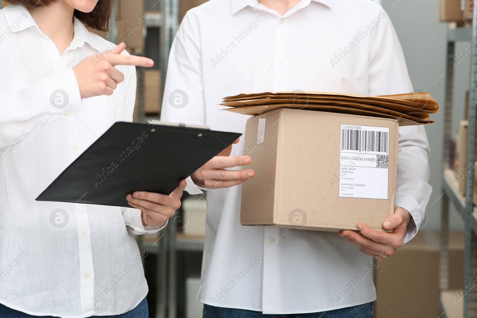 Photo of Post office workers checking parcel barcode near rack indoors, closeup