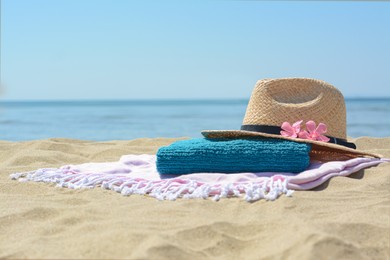Blanket with towel, stylish straw hat and flowers on sand near sea, space for text. Beach accessories