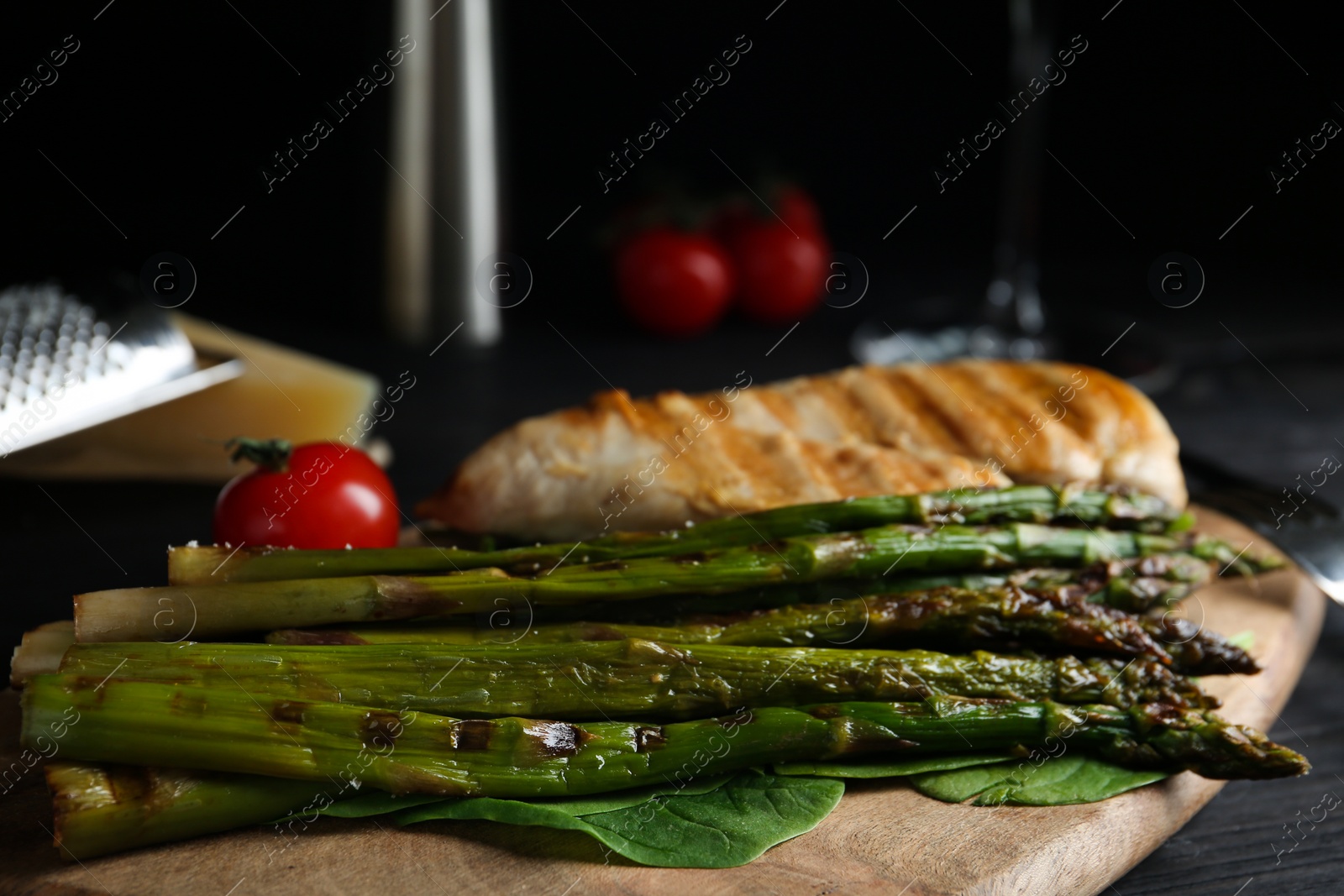 Photo of Tasty grilled chicken fillet served with asparagus on wooden board, closeup