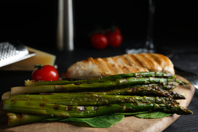 Tasty grilled chicken fillet served with asparagus on wooden board, closeup