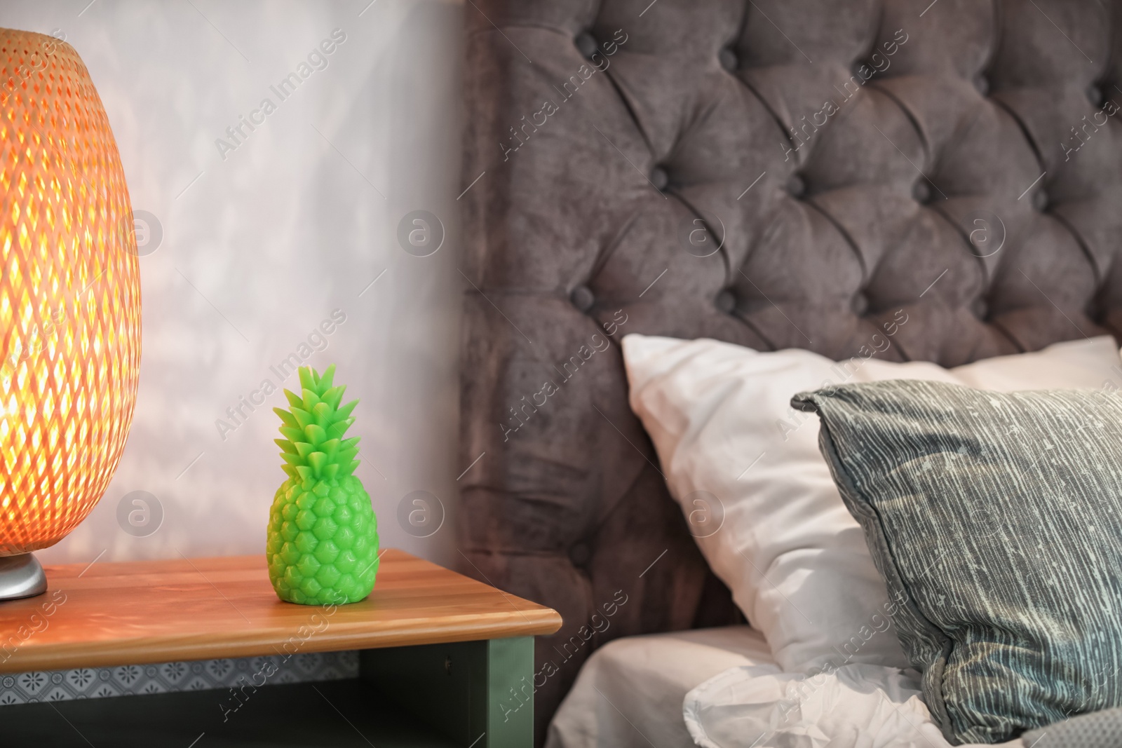 Photo of Pineapple shaped candle and lamp on bedside table in room