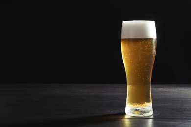 Photo of Glass with cold tasty beer on dark background