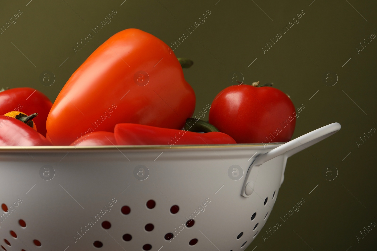 Photo of Colander with fresh vegetables on olive background, closeup