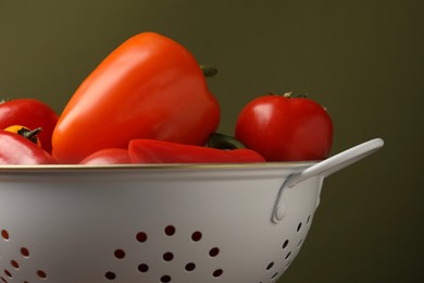 Photo of Colander with fresh vegetables on olive background, closeup