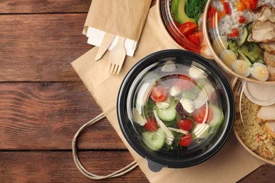 Tasty food in containers with knife and fork on wooden table, flat lay. Space for text