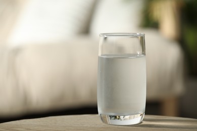Glass of pure water on wooden table against blurred background, space for text