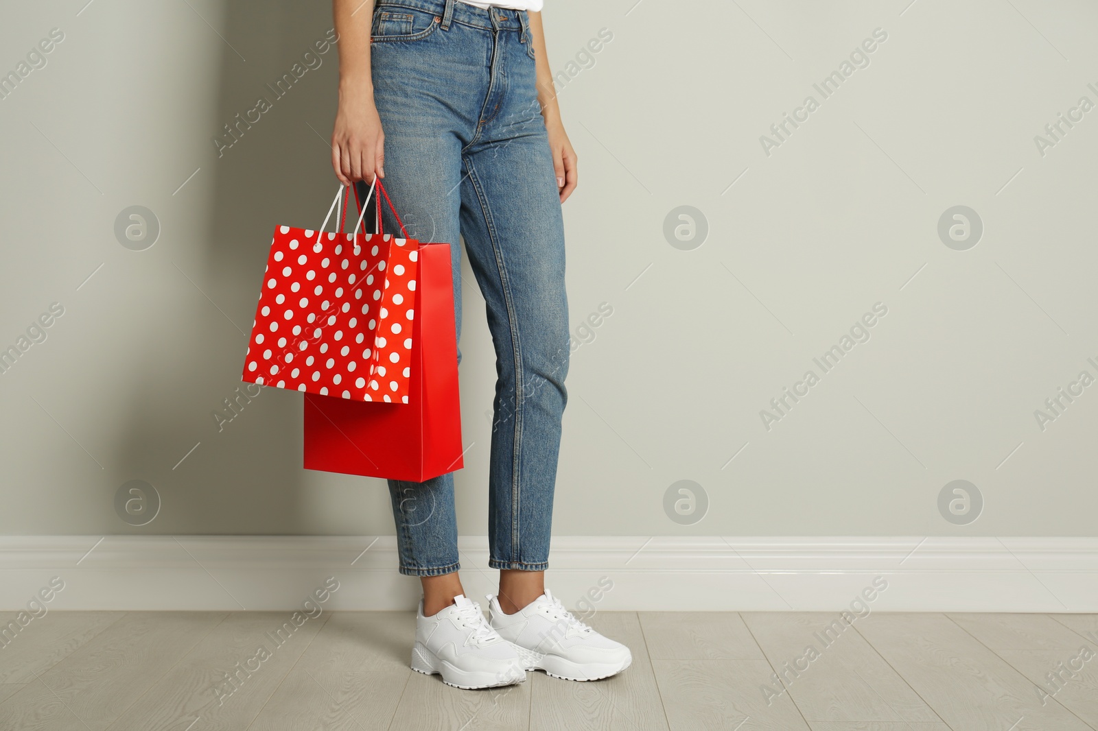 Photo of Woman with paper shopping bags near light grey wall, closeup. Space for text