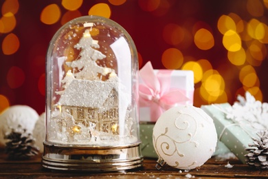 Beautiful snow globe, Christmas bauble and gifts on wooden table against blurred festive lights