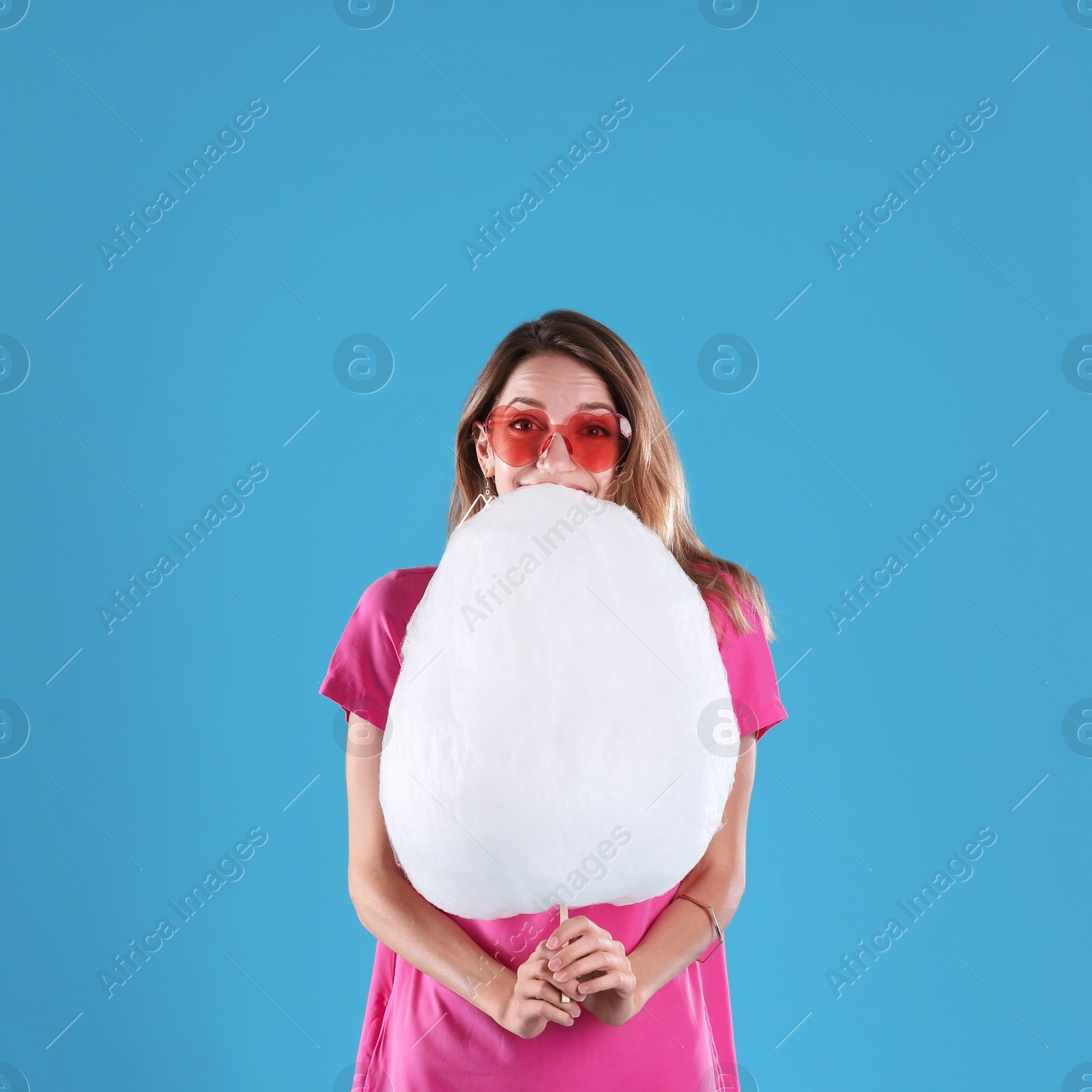 Photo of Happy young woman with cotton candy on blue background