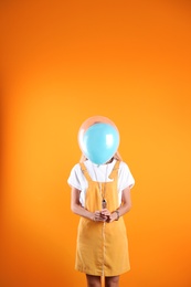 Young woman hiding behind air balloon on color background