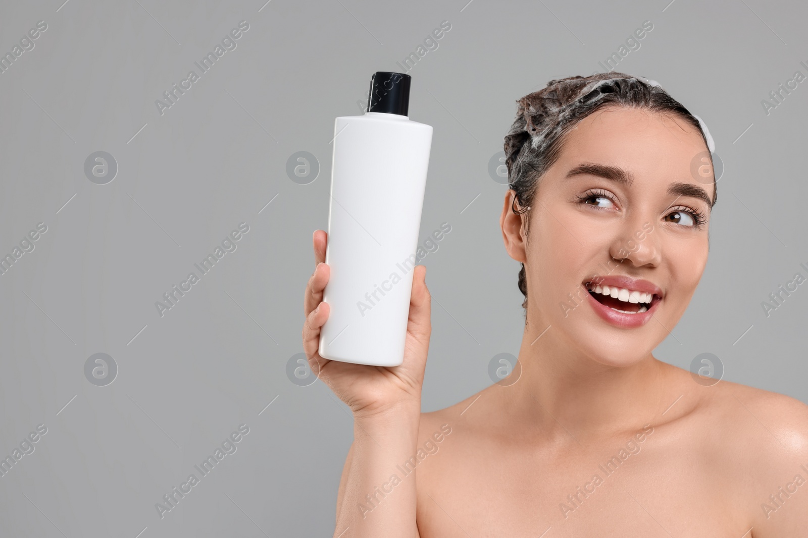 Photo of Washing hair. Portrait of beautiful happy woman with bottle on grey background. Space for text