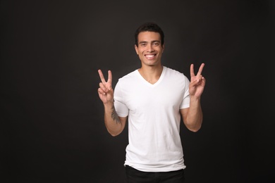 Handsome young African-American man showing victory gesture on black background