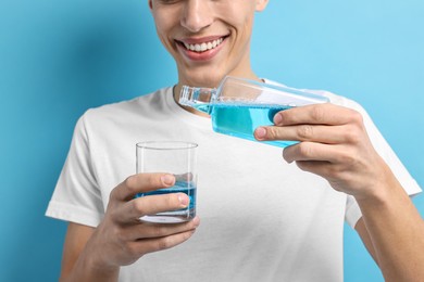 Photo of Young man using mouthwash on light blue background, closeup