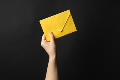 Photo of Woman holding yellow paper envelope on black background, closeup