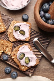 Photo of Tasty sandwiches with cream cheese and blueberries on wooden table, flat lay