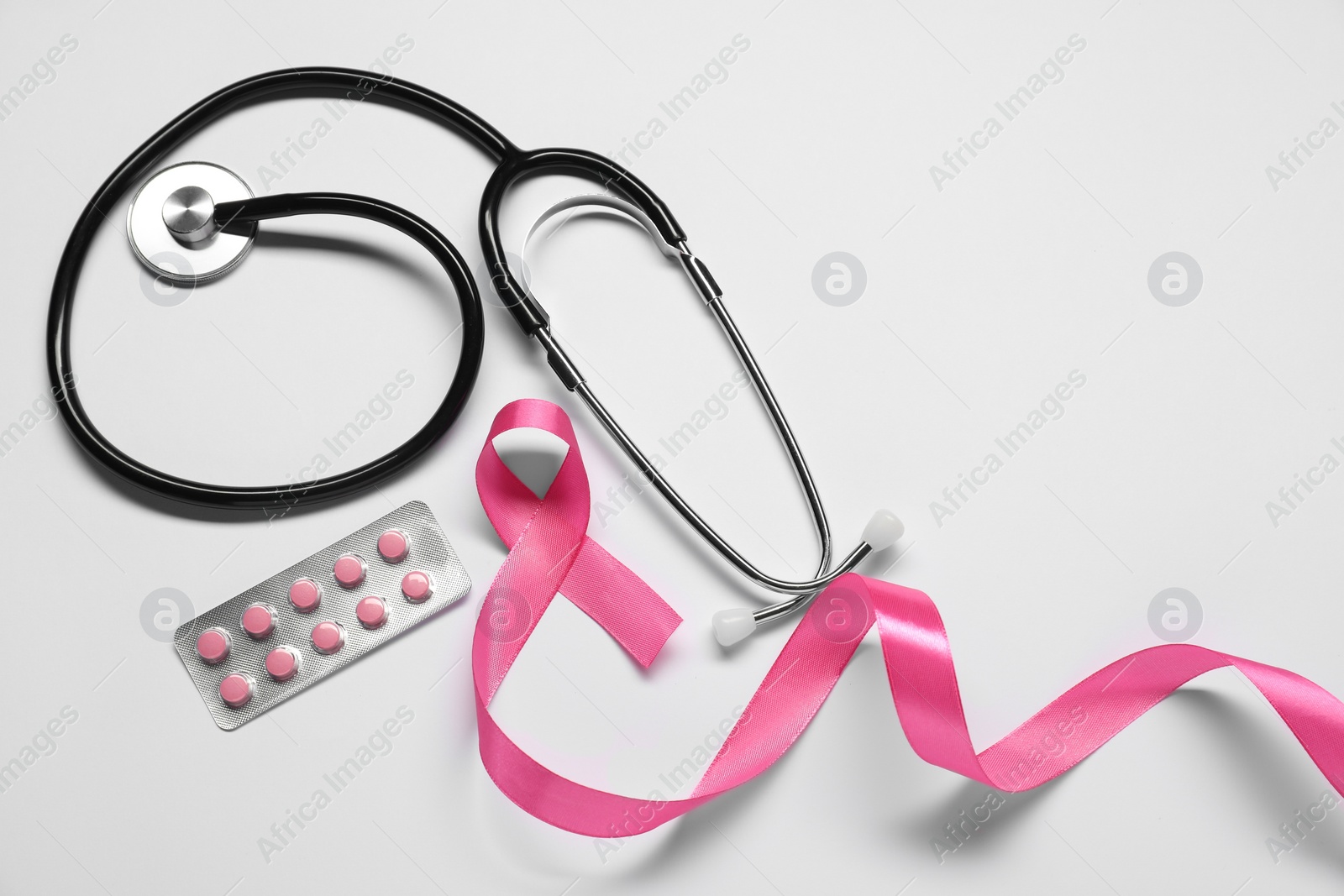 Photo of Breast cancer awareness. Pink ribbon, stethoscope and pills on white background, flat lay. Space for text