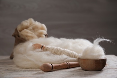 Photo of Soft white wool and spindles on wooden table. Space for text