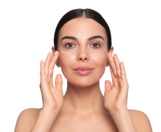 Photo of Beautiful young woman with cream on skin under eye against white background