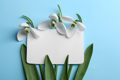 Beautiful snowdrops and paper card on light blue background, flat lay. Space for text