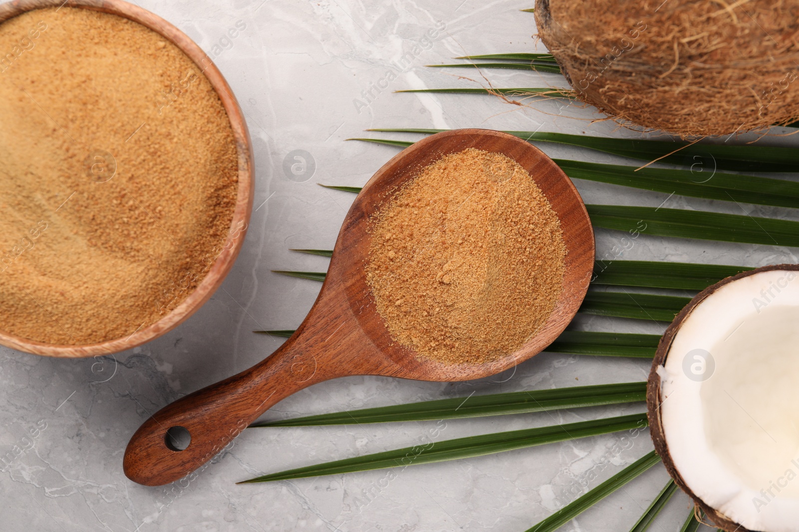 Photo of Spoon with coconut sugar, palm leaves, bowl and fruits on grey marble table, flat lay