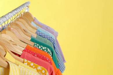 Photo of Bright clothes hanging on rack against yellow background, space for text. Rainbow colors