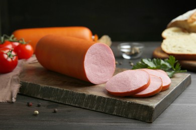 Photo of Board with tasty boiled sausage on dark wooden table, closeup