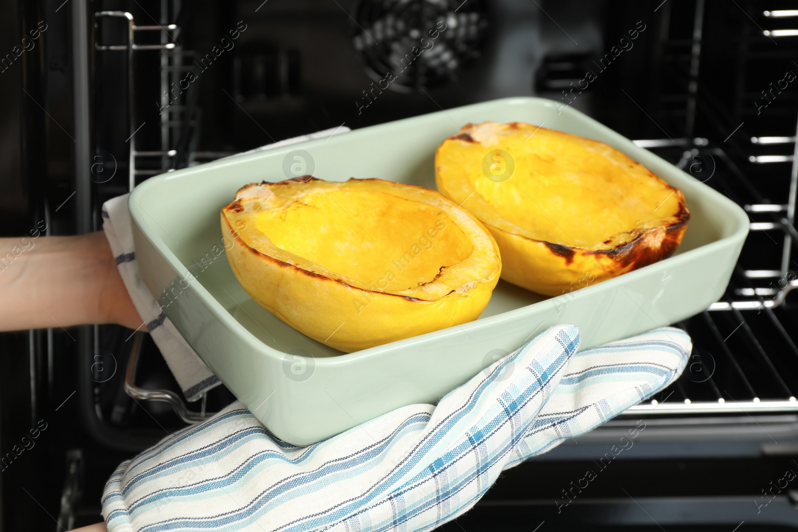 Photo of Woman taking baked spaghetti squash out of oven, closeup