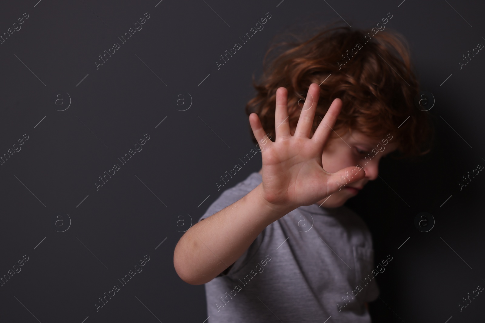 Photo of Child abuse. Boy making stop gesture near grey wall, selective focus. Space for text