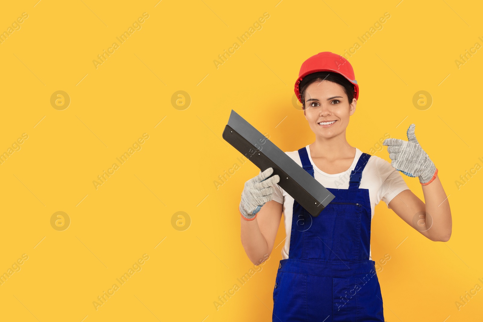 Photo of Professional worker with putty knife in hard hat on orange background, space for text