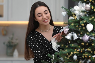 Smiling woman decorating Christmas tree with bow indoors