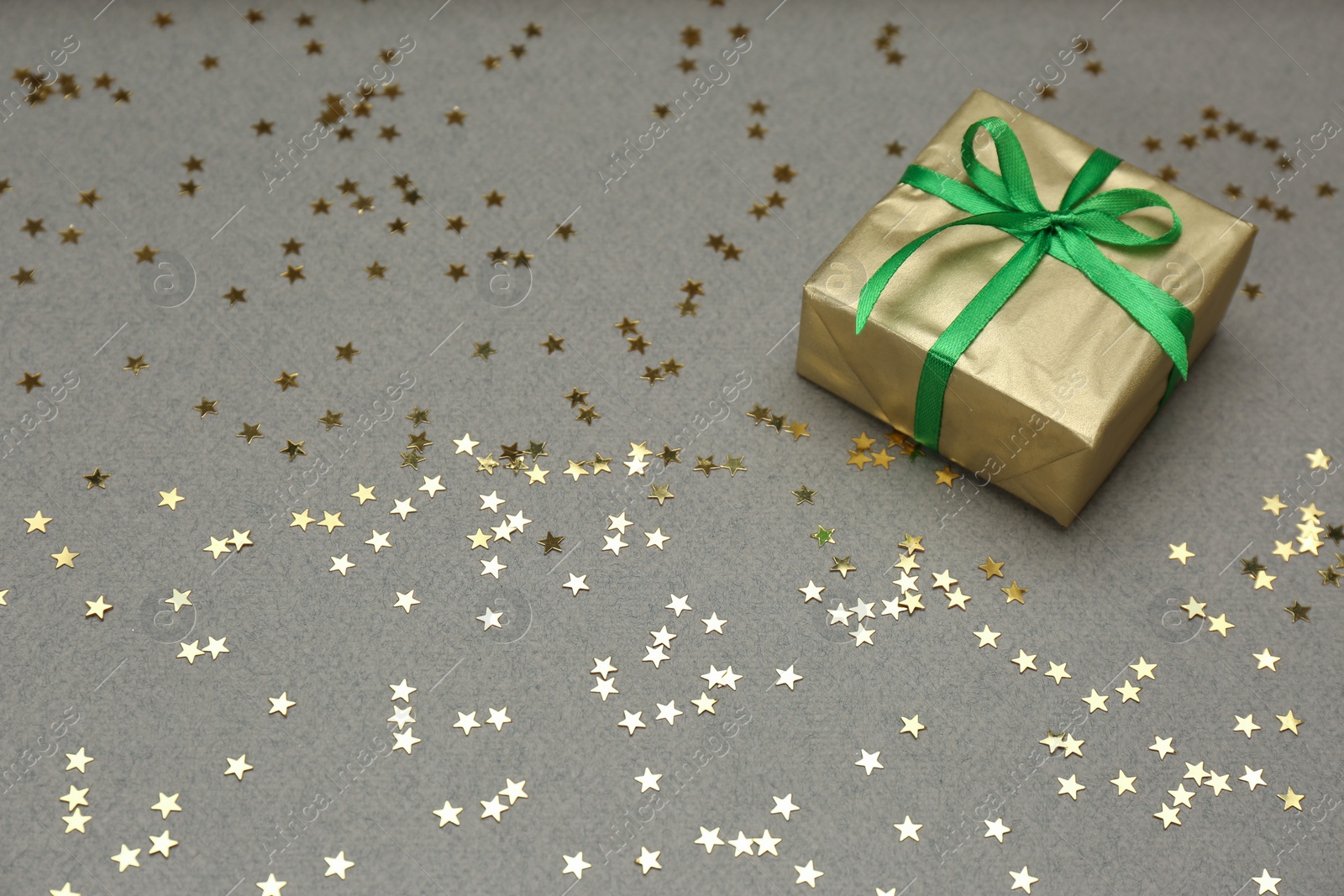 Photo of Golden gift box and shiny confetti on grey background, space for text