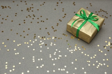 Photo of Golden gift box and shiny confetti on grey background, space for text