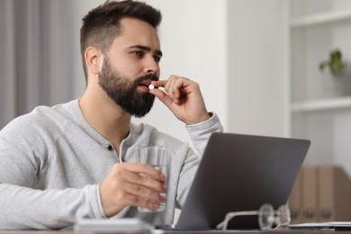 Young man taking pill against headache in office