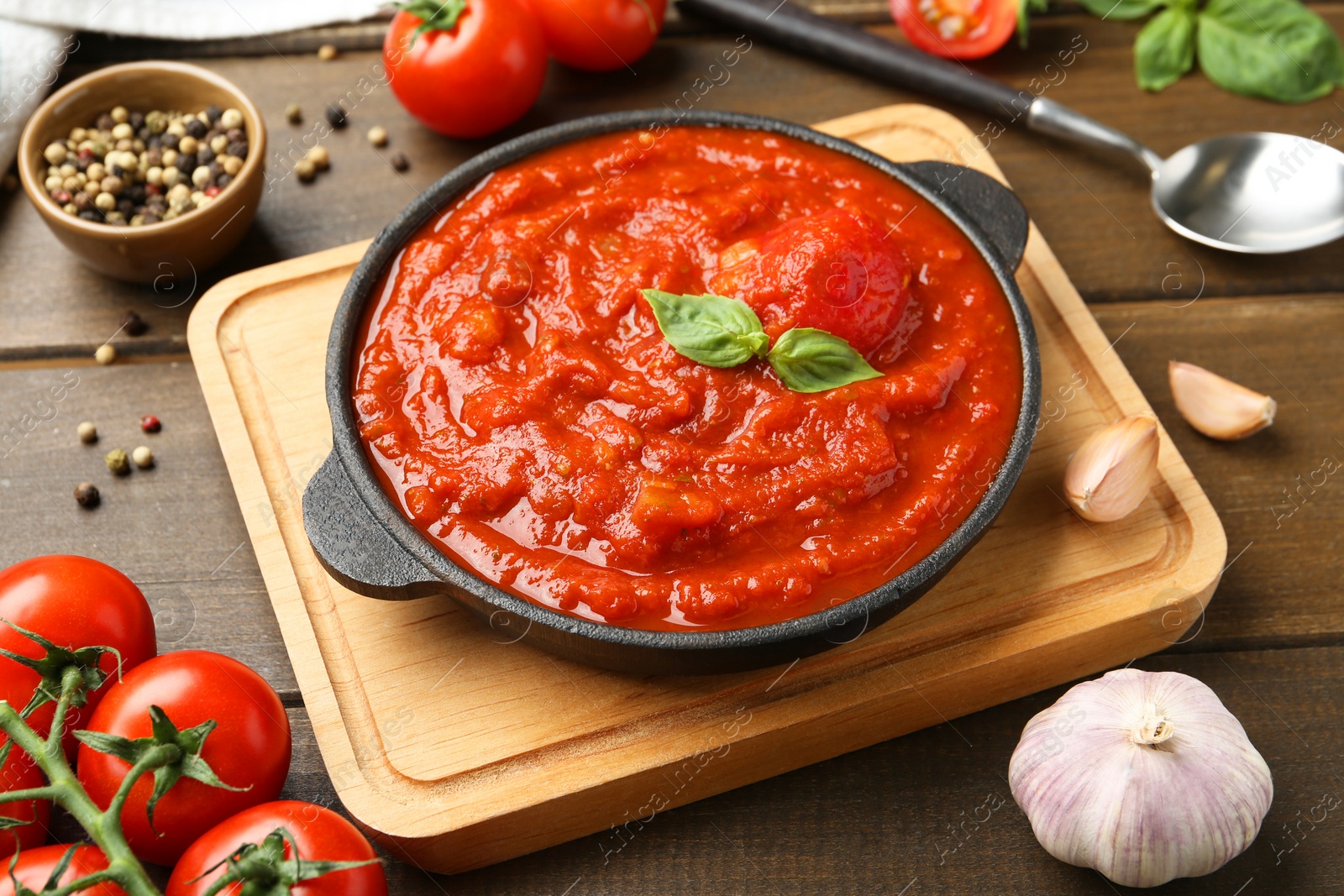 Photo of Homemade tomato sauce in bowl, spoon and ingredients on wooden table